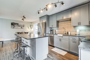 Eine moderne Küche mit grauen Schränken, einem Edelstahl-Kühlschrank und einer Bar mit Hockern.