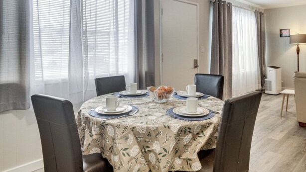 Un comedor con una mesa redonda preparada para cuatro personas, rodeada de sillas.