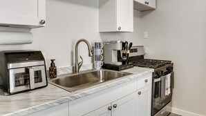 Una cocina moderna con armarios blancos, un lavamanos de acero inoxidable, una cafetera y un horno empotrado.