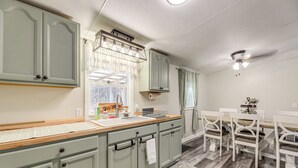 Una cocina con armarios verde claro, una encimera de madera y una zona de comedor con sillas blancas y una mesa.