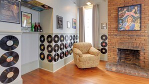 Ein Zimmer mit Kamin aus Ziegelsteinen, einem gemusterten Sessel und einer Wand voller Schallplatten.