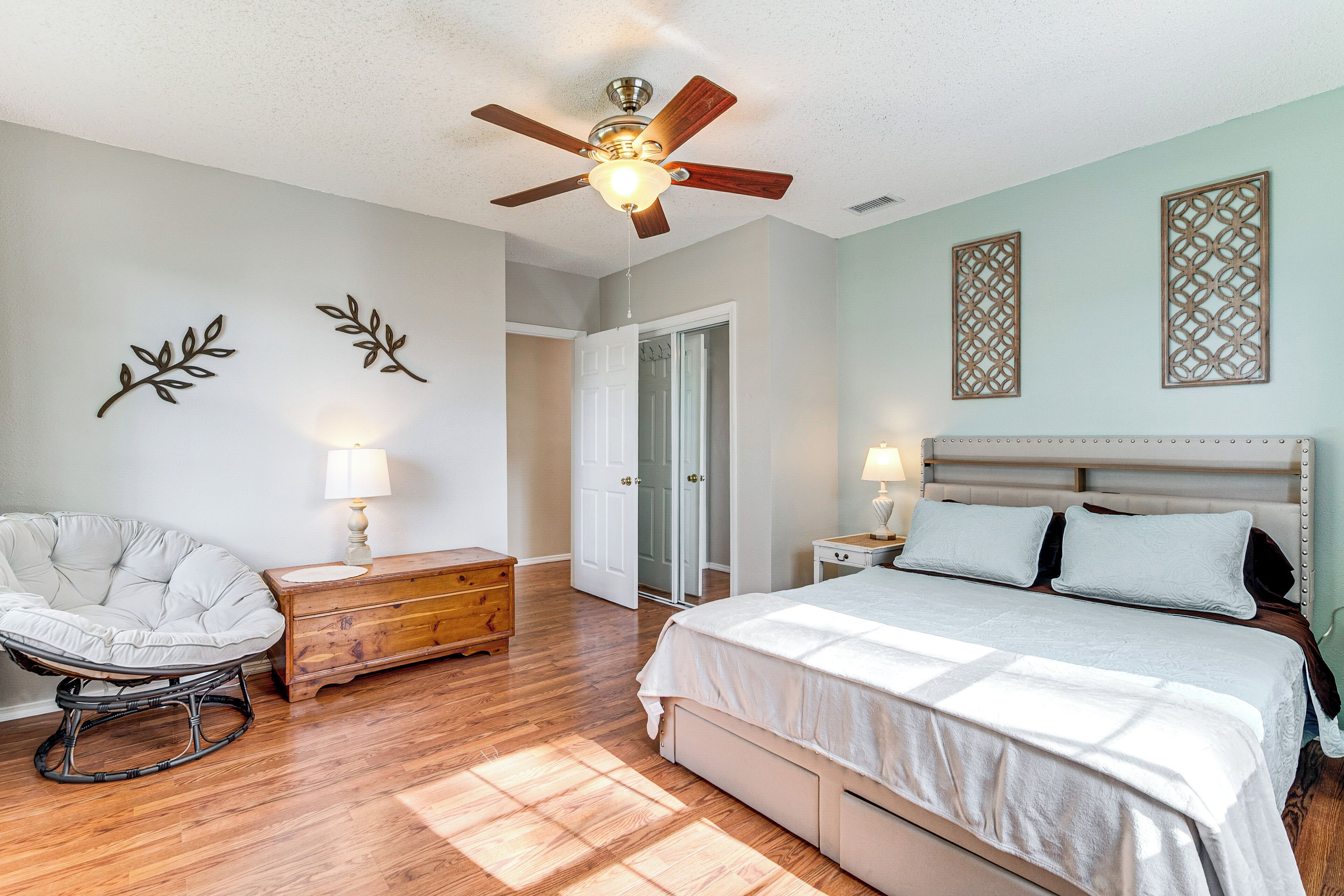 A bedroom with a bed, a ceiling fan, a chair, a dresser, and decorative wall art.
