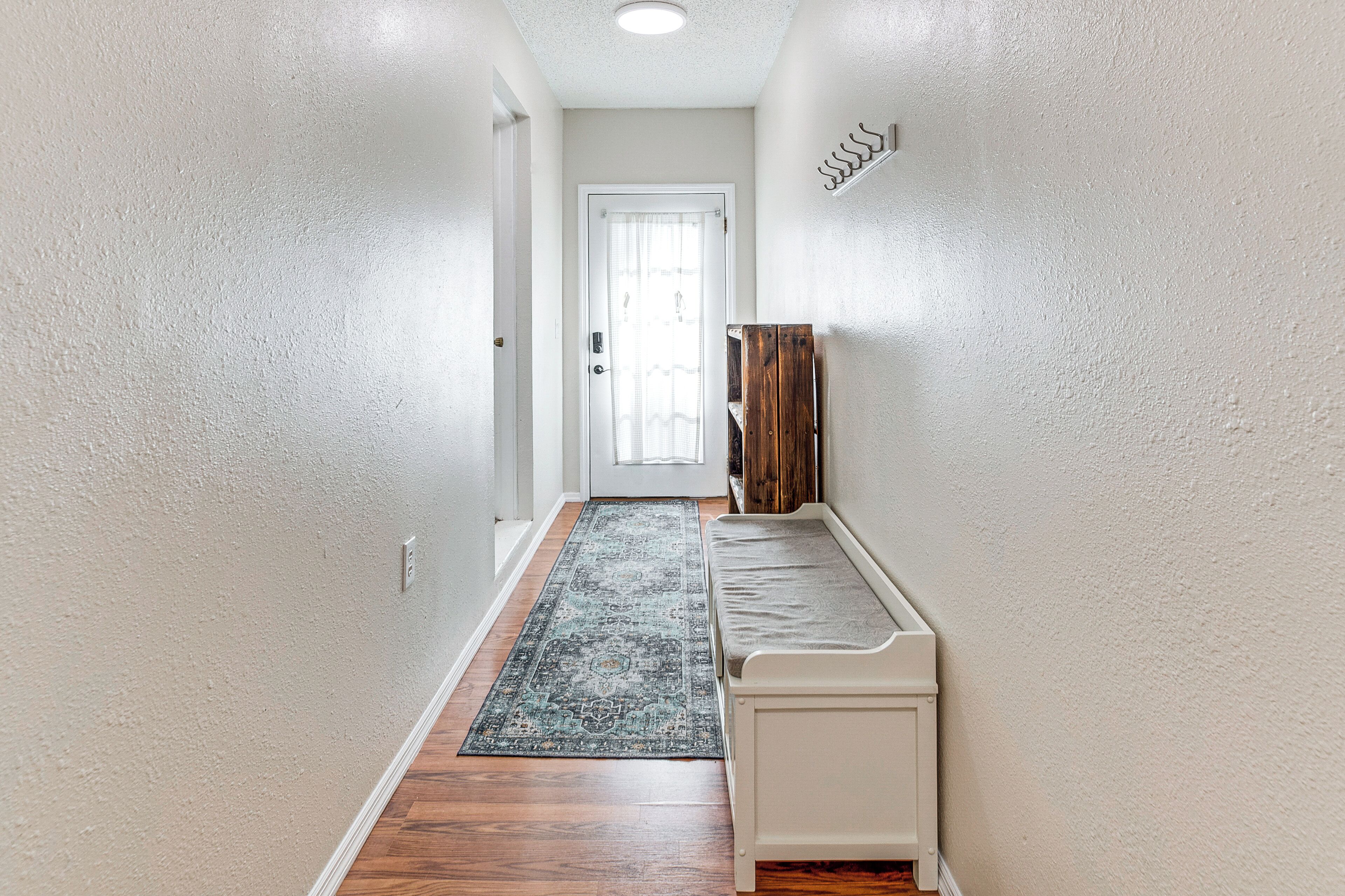 A narrow hallway with a bench, a patterned rug, and a door at the end.