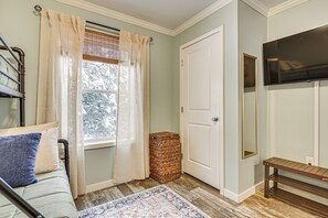A room with a bed, a window with curtains, a door, a television, and a mirror.