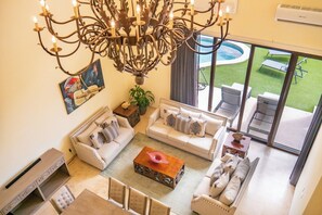 A spacious living area with a large chandelier, two sofas, a coffee table, and a view of a swimming pool through large windows. - Spacious 4-bedroom villa in fantastic Cabo San Lucas with AC (Cabo San Lucas)