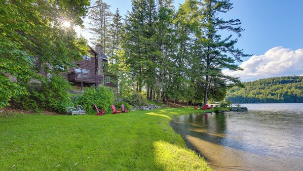 Un chalet au bord du lac, doté d’une terrasse, entouré d’une végétation luxuriante et offrant une vue dégagée sur le lac.