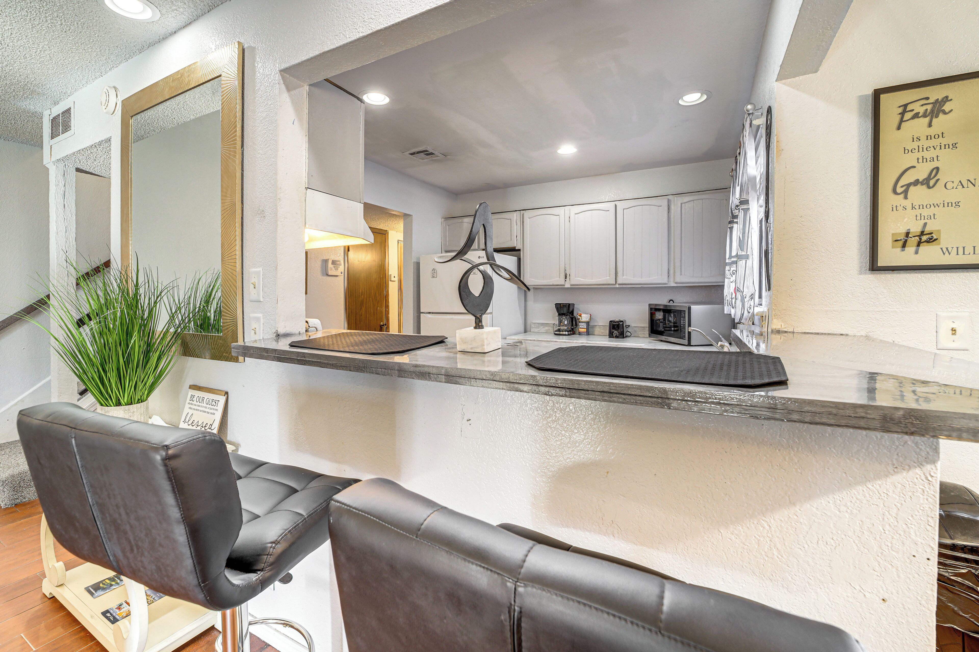 Una cocina moderna con armarios blancos, un lavamanos de acero inoxidable y una zona de bar con una silla de cuero negro.