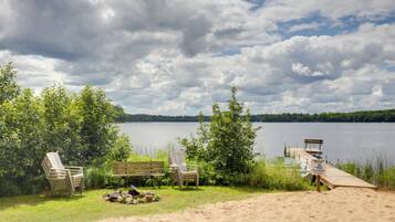 A lakeside setting with a wooden deck, lounge chairs, and a sandy area.