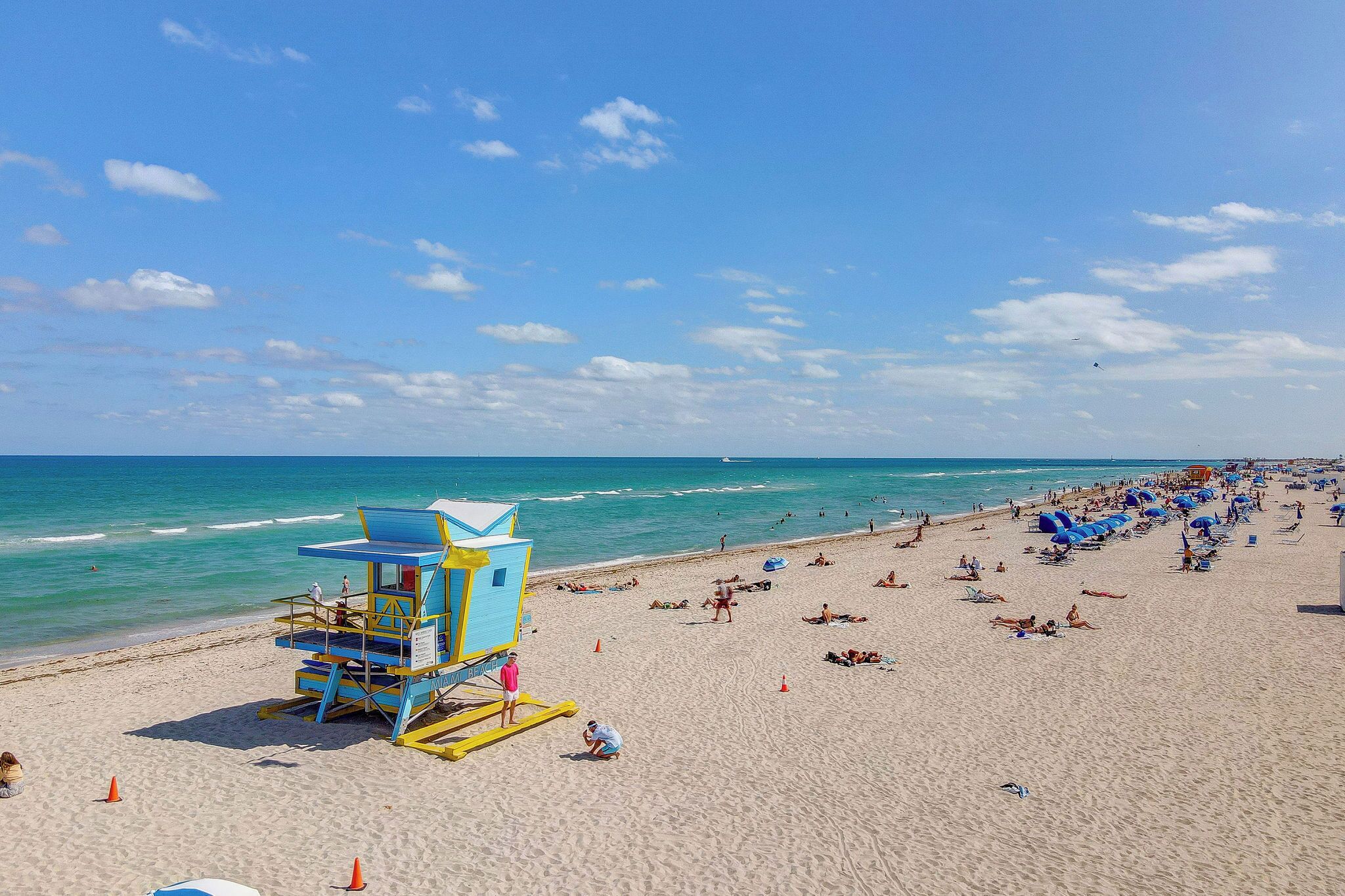 A beach with lifeguard towers, umbrellas, and people sunbathing.