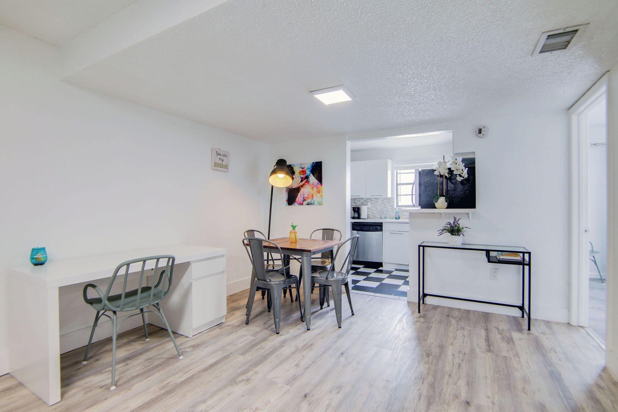 A modern kitchen with white cabinets, a black and white checkered floor, and a dining area with a wooden table and metal chairs.