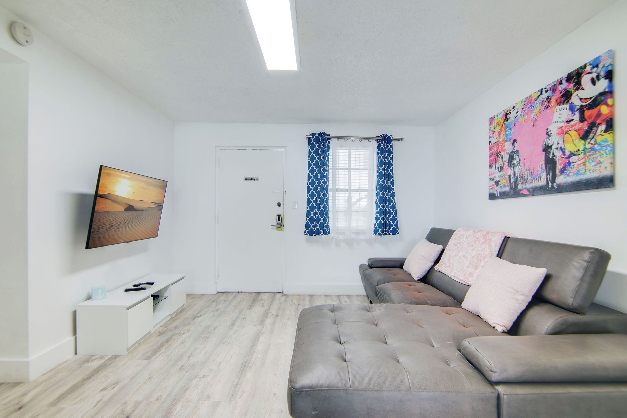 Ein modernes Wohnzimmer mit grauem Sofa, Flachbildfernseher und einem Bild an der Wand.
