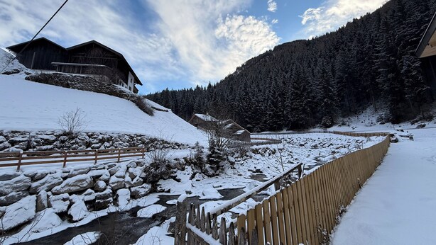 Paisaje nevado con casas de madera, un muro de piedra y una valla de madera.