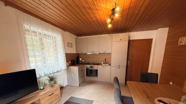 Cocina compacta con comedor, televisión y techo de madera.