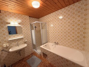 A bathroom with patterned wallpaper, a wooden ceiling, a glass shower enclosure, and a large bathtub.
