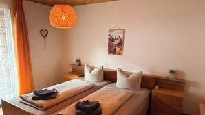 Una cama doble con dos almohadas, una mesita de noche con una planta, una lámpara colgante y un cuadro en la pared.