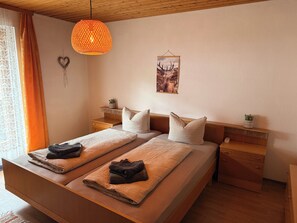 A double bed with two pillows, a bedside table with a plant, a hanging light fixture, and a wall-mounted picture.