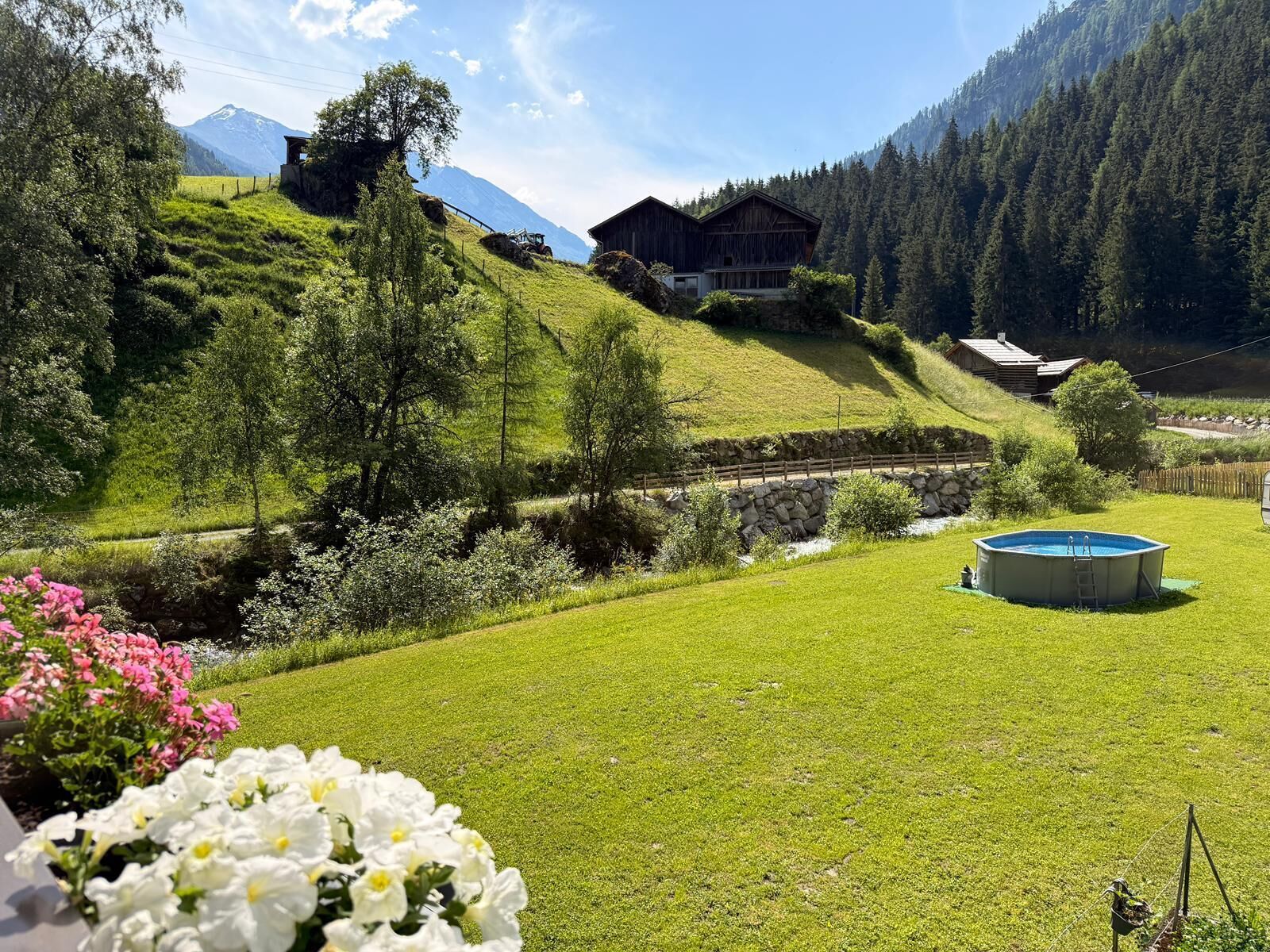 A rural landscape with a swimming pool, a wooden cabin, and a mountain in the background.