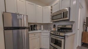 A compact kitchen with white cabinets, a stainless steel refrigerator, a microwave, a stove, and a coffee maker. - Simple Studio -Walk to MGH, Beacon Hill, North End (Boston)