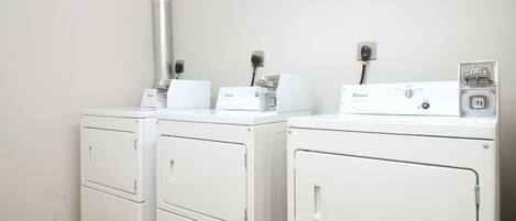 A laundry room with two white Whirlpool washers and dryers, a metal vent, and a power outlet on the wall.
