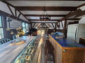 A rustic kitchen with exposed wooden beams, a stone fireplace, and a modern refrigerator.