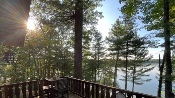 A wooden deck with a table and chairs, overlooking a lake surrounded by trees. - Chalet on the Lake, Fireplace, Washer/Dryer, Snowmobile, ATV, Sleeps 8 (Woodruff)