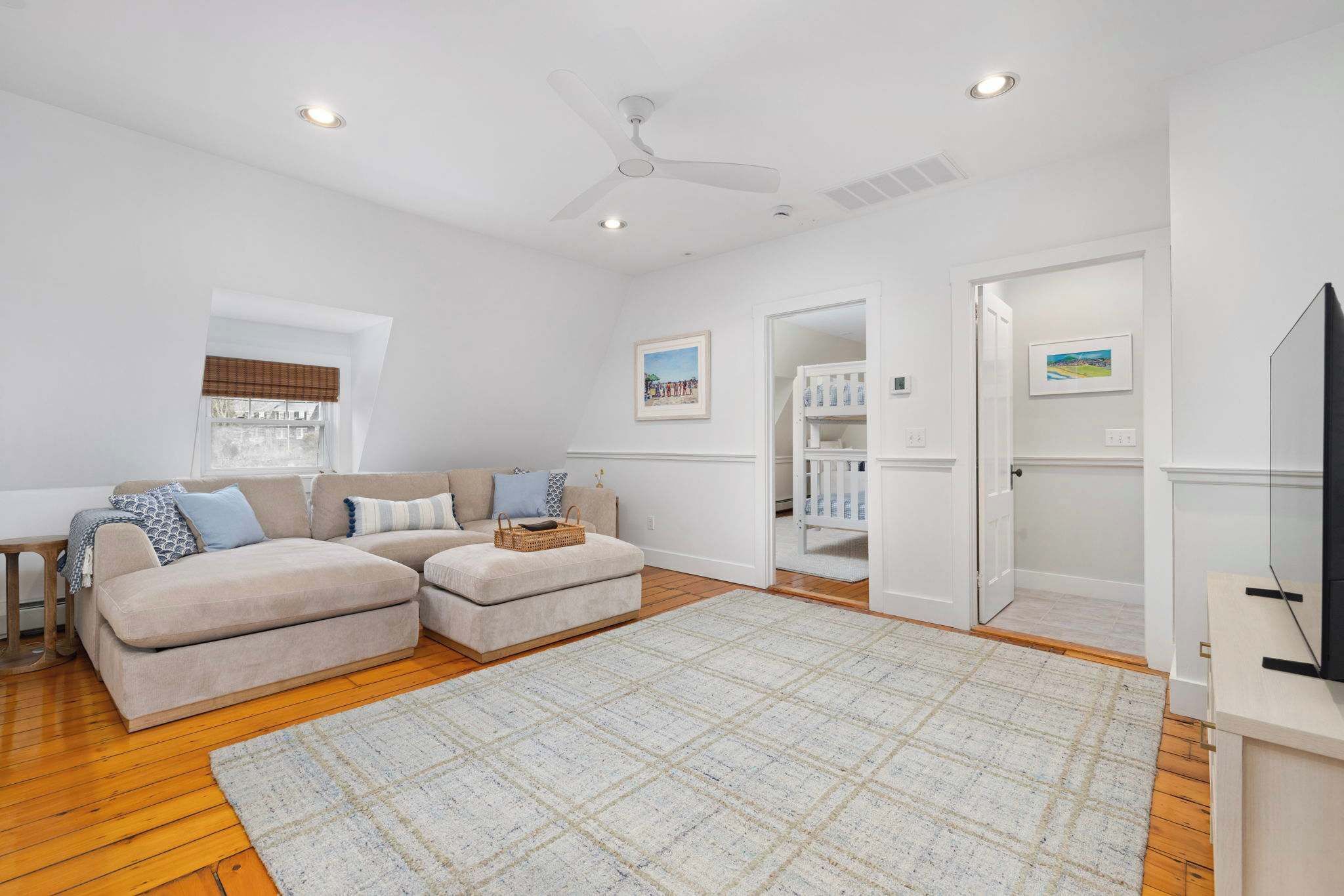 A spacious living room with a beige sofa, ottoman, and a large rug. There is a ceiling fan, recessed lighting, and a door leading to a closet.
