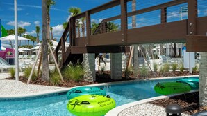 Un espace piscine avec des bouées gonflables, des palmiers et un pont en bois.