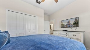 Un dormitorio con una cama grande, un aparador, un televisor y una puerta que da a otra habitación.