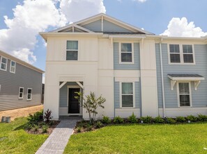 A two-story residential building with a front entrance, a small porch, and a pathway leading to the door. - Magical 5Bd Themed w/ Waterpark Near Disney 16161 (Clermont)