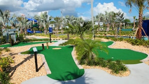 Un parcours de golf avec un green bien entretenu, des palmiers et une toboggan aquatique en arrière-plan.