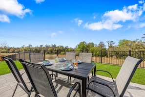 Une terrasse extérieure avec une table dressée pour le repas, entourée de chaises, et offrant une vue sur le ciel et les arbres.
