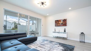 Un salon moderne avec un canapé d’angle, une grande fenêtre, un tableau et un meuble blanc.