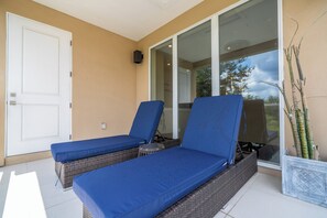 Une pièce comprenant deux fauteuils de relaxation en osier avec des coussins bleus, une porte blanche et une porte vitrée donnant sur l’extérieur.