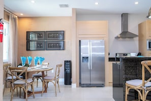 A modern kitchen with a stainless steel refrigerator, wooden cabinets, and a dining area with wicker chairs. - Modern Magic Village Home for 8 with Grill 3131 (Kissimmee)