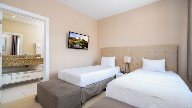 Una camera d'albergo con due letti, un bagno con uno specchio e un lavandino, e una TV a parete.