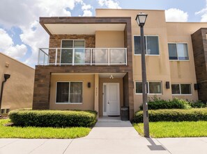 A modern two-story building with a balcony, a door, and a trash bin. - Modern Magic Village Home for 8 with Grill 3131 (Kissimmee)