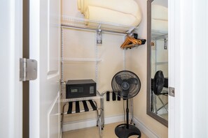 Une pièce avec une porte blanche, une étagère en métal sur laquelle se trouve une radio noire, un ventilateur sur pied et un miroir qui reflète une partie de la pièce.