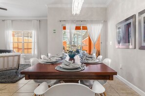 A dining room with a wooden table set for six, white chairs, a chandelier, and a view through large windows. - Paradise 4Bd w Private Pool & Waterpark 2941 (Kissimmee)
