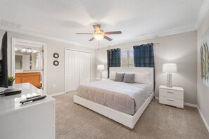 A bedroom with a bed, nightstands, a desk, a ceiling fan, and a door leading to a bathroom. - Paradise 4Bd w Private Pool & Waterpark 2941 (Kissimmee)