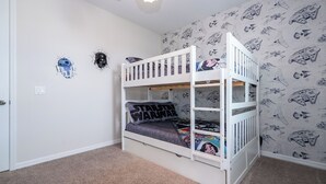 Un lit superposé avec une literie aux motifs de Star Wars, un mur recouvert d’un papier peint Star Wars et un sol recouvert de moquette.