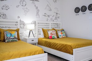 A room with two beds, a white nightstand, a lamp, and a wall decorated with travel-themed stickers. - Stunning 4Bd w Pool Gameroom Solara Resort 9008 (Kissimmee)