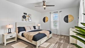Een slaapkamer met een bed, nachtkastjes, een plafondventilator en wanddecoratie.