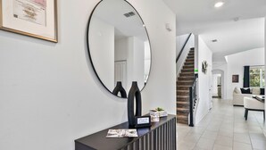 Een modern interieur met een grote, ovale spiegel, een donkere consoles met decoratieve voorwerpen, een trap en een zithoek met een bank.