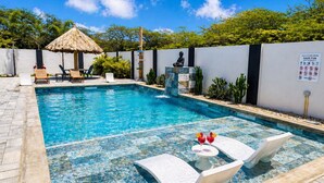 A swimming pool with lounge chairs and a thatched-roof structure. - Luxury 6BR Villa Near Eagle Beach with Pool, Volleyball & Putting Green (Oranjestad)