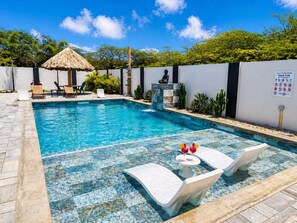 A swimming pool with lounge chairs and a thatched-roof structure. - Luxury 6BR Villa Near Eagle Beach with Pool, Volleyball & Putting Green (Oranjestad)