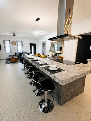 A modern kitchen with a long island, bar stools, and a large mirror. - Luxury 6BR Villa Near Eagle Beach with Pool, Volleyball & Putting Green (Oranjestad)