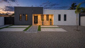 A modern house with a dark facade, a stone accent wall, and a well-lit entrance. - Luxury 6BR Villa Near Eagle Beach with Pool, Volleyball & Putting Green (Oranjestad)