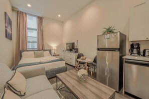 Una habitación de hotel moderna con cama, una pequeña mesa de comedor, un refrigerador y una kitchenette.