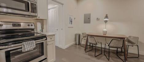 A modern kitchen with a microwave, oven, and dining area with chairs and a table.
