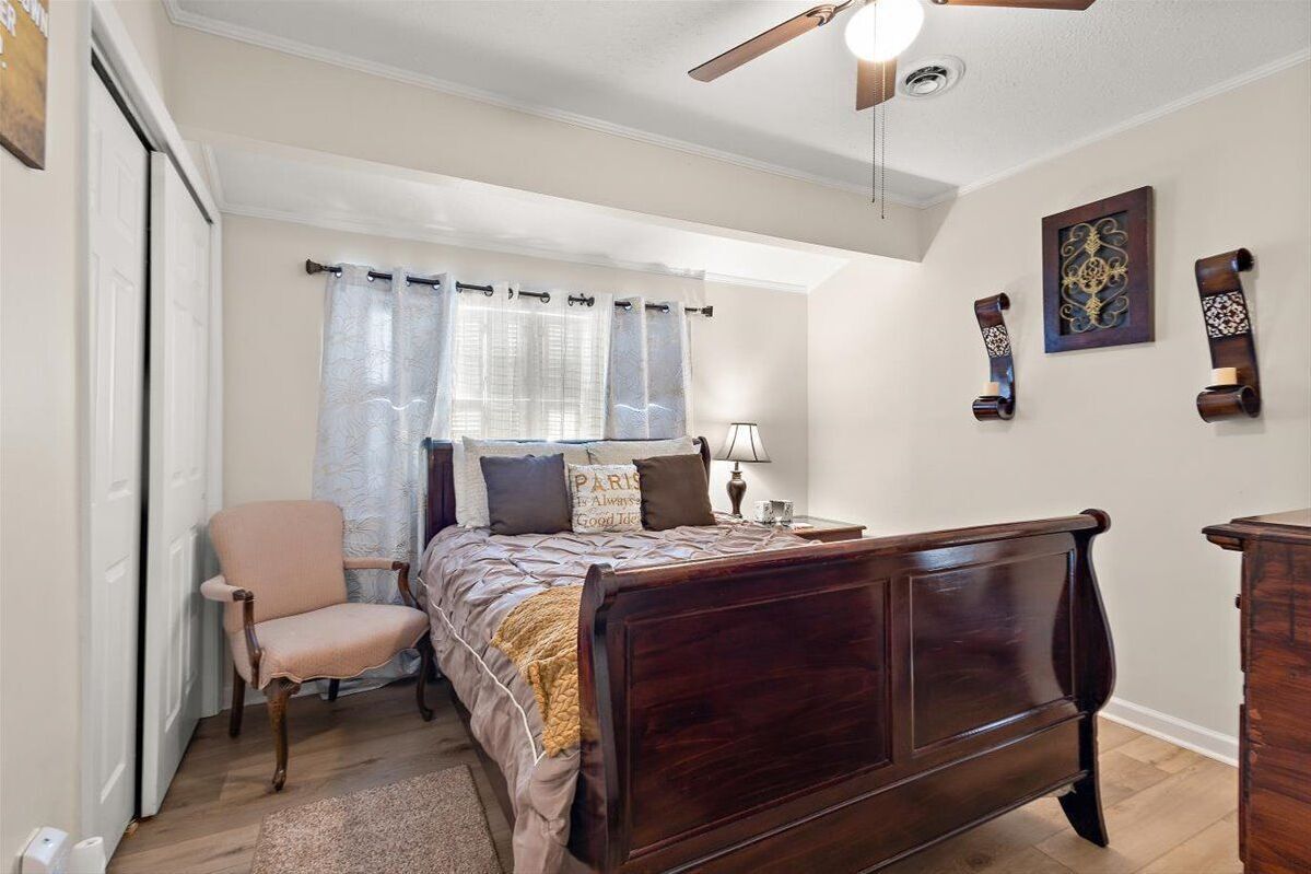 A bedroom with a wooden bed, a chair, a nightstand, a lamp, and a ceiling fan.